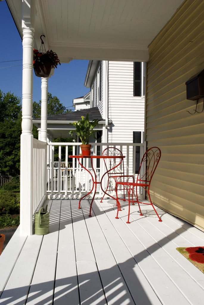Freshly painted front porch with white railings and two red bistro chairs