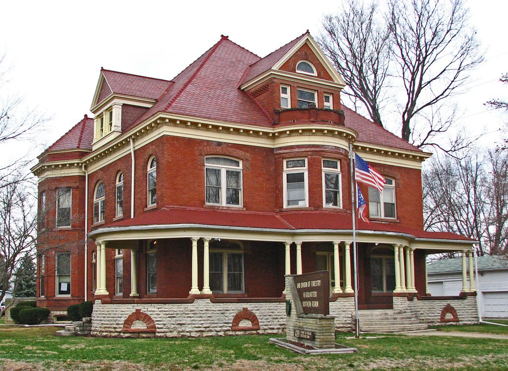 Red brick Victorian house with a wide wraparound porch and a green lawn