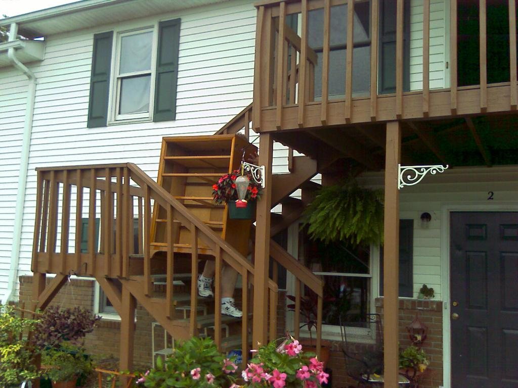 Wooden outdoor staircase decorated with hanging flower baskets beside a white house
